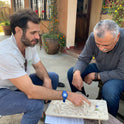 Two men sit at an outdoor table playing with The Oort Cloud – Wooden Marble Run Puzzle.