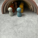 Colorful, minimalist Silicone Mini Peg Dolls (Set of 6) arranged in front of and underneath a nested, arched stacker toy, perfect for pretend play.