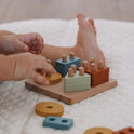 A child’s hands play with a Montessori Wood & Silicone Shape Puzzle, using blue, yellow, green, and orange wooden geometric shapes to build fine motor skills.