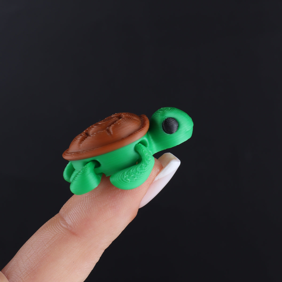 A small green and brown Micro Animal Fidgets – Surprise Pack turtle balanced on a fingertip as cute mini desk decor.