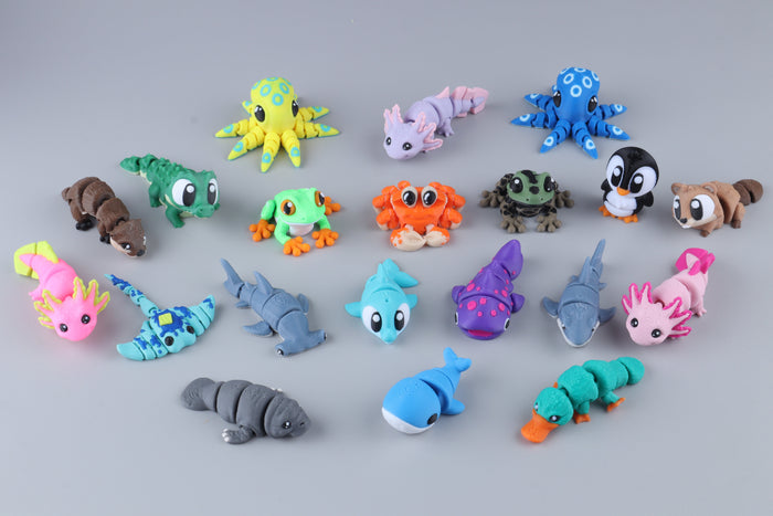 A 20-pack of Mini Water Animal Fidgets featuring twenty small, colorful, 3D-printed articulated sea creatures, amphibians, and a penguin arranged on a gray surface.