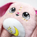 Close-up of Mylo the Moon Pal – 5 lb Weighted Plush, an ultra-soft pink rabbit with large embroidered eyes, yellow accents, and a crescent moon with stars on its belly, designed as a calming hug.