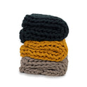 Three Knit Weighted Blankets are stacked: a dark green super soft weighted blanket on top, mustard yellow in the middle, and light taupe on the bottom—each features thick, braided yarn textures for cozy warmth.