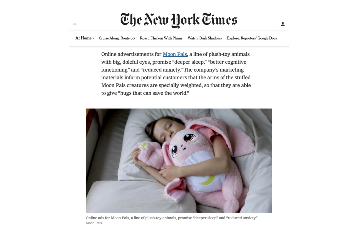 A child sleeps in bed, enjoying a calming hug while embracing a Mylo the Moon Pal – 5 lb Weighted Plush, an ultra-soft toy with large eyes and a moon emblem on its belly.