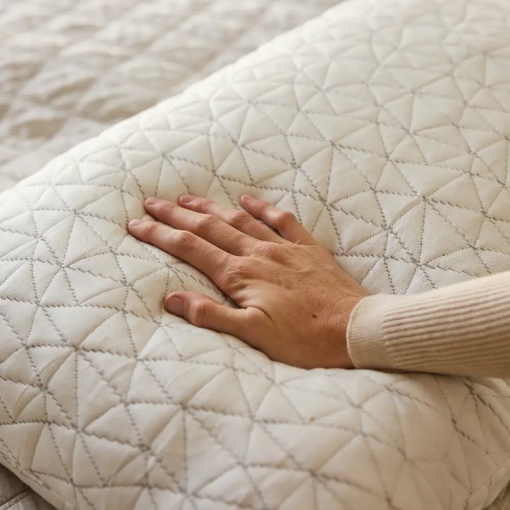 A hand presses down on a Cloud Adjustable Memory Foam Pillow with a white, quilted cover featuring a geometric pattern, highlighting its premium softness and texture.