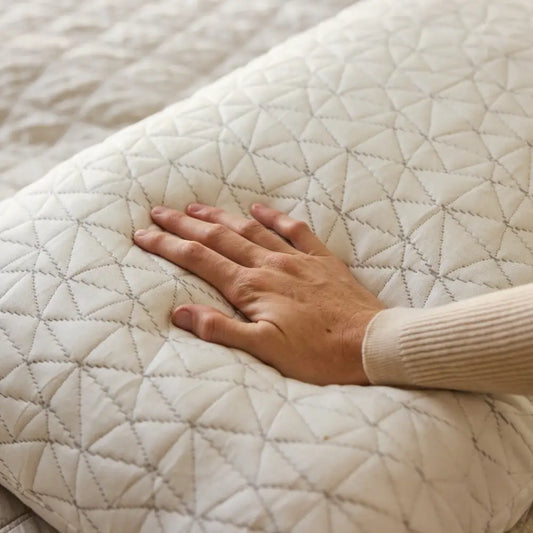A hand presses down on a Cloud Adjustable Memory Foam Pillow with a white, quilted cover featuring a geometric pattern, highlighting its premium softness and texture.