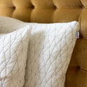 Two Cloud Adjustable Memory Foam Pillows in classic white, featuring a quilted geometric pattern, are arranged against a mustard yellow tufted headboard. Offering premium softness, this set of two includes a small fabric tag on one pillow that reads “nuzzle.”.