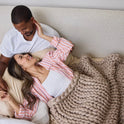 A couple relaxes in bed, smiling at each other. The woman cozily rests under the Ice Knit Weighted Blanket, her hand gently on the mans face. Both look content and happy, sharing an intimate moment wrapped in comfort.
