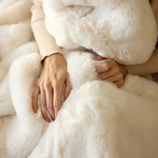 A person drapes themselves in the Snuggle Luxe Blanket, their hands resting on its soft, plush fabric, while wearing a beige sweater.