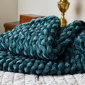 A plush Velvet Weighted Blanket in teal rests on a white quilted bedspread, bringing cozy comfort to the room, with a brass lamp and wooden furniture visible in the background.