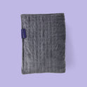 A folded dark gray Gravity Original Weighted Blanket (10–25 lb) with a breathable cover, a stitched grid pattern, and a small rectangular brand tag on the side.