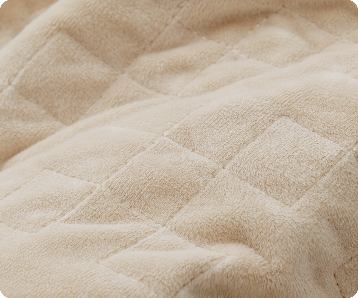 Close-up of a tan Gravity Original Weighted Blanket (10–25 lb) with a quilted square pattern and breathable cover.