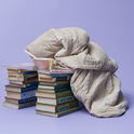 A Gravity Original Weighted Blanket (10–25 lb) with a breathable quilted cover draped over two stacks of books and a small bowl of noodles.