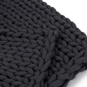 A close-up of the Knit Weighted Blanket, a chunky, black hand-knitted blanket made from thick, soft yarn for breathability, shown against a white background.