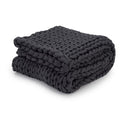 A chunky, hand-knit Knit Weighted Blanket in charcoal, featuring a braided design and thick yarn, is folded neatly on a white background.