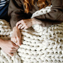 Two people sit close together, holding hands under the Knit Weighted Blanket. Only their hands, arms, and part of their torsos are visible, creating a cozy and intimate atmosphere.