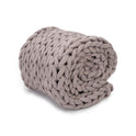 The Knit Weighted Blanket, in chunky light gray, is rolled up to show off its thick braided texture and ultra-soft, cozy look against a white background.
