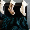 Three Christmas stockings hang above a dark fireplace, with a Knit Weighted Blanket in chunky, dark green knit draped super softly in front of the hearth.