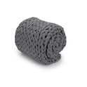 The Knit Weighted Blanket, featuring a chunky dark gray braided design, is rolled up on a white background.