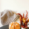 A cozy scene with a Knit Weighted Blanket draped over a white sofa. In the foreground, a ceramic pumpkin and a vase of autumn-hued dried flowers rest on a table.