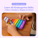 A child’s hands hold a rainbow-colored silicone pop-it toy and a phonics card from the Rising Reader Game Bundle featuring a unicorn and geometric shapes.