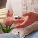 A person in a light shirt holds and opens the ONO Roller Steel compact flip phone with both hands, with a blurred green plant serving as desk decor in the background.