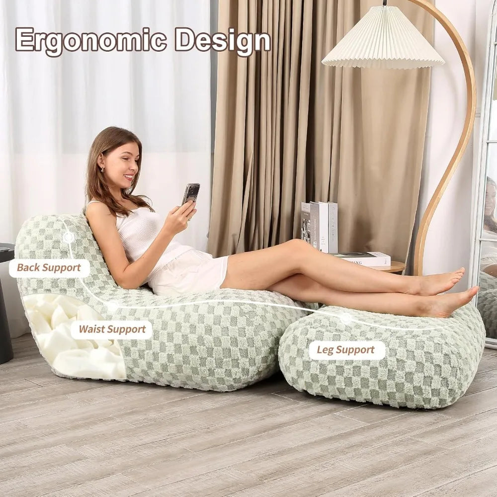 A woman relaxes on the Bean Bag Chair with Footstool, a comfy memory foam lounge for adults providing back, waist, and leg support. The modern sofa is set in a living room with a floor lamp, curtains, and shelf nearby.