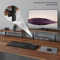 The Standing Desk w/ 2 Adjustable Monitor Shelves Electric Stand Up Desk holds a monitor, camera, phone, and organizer. A keyboard, mouse, and mouse pad are on the wooden surface. A digital clock shows February 12, 12:59.