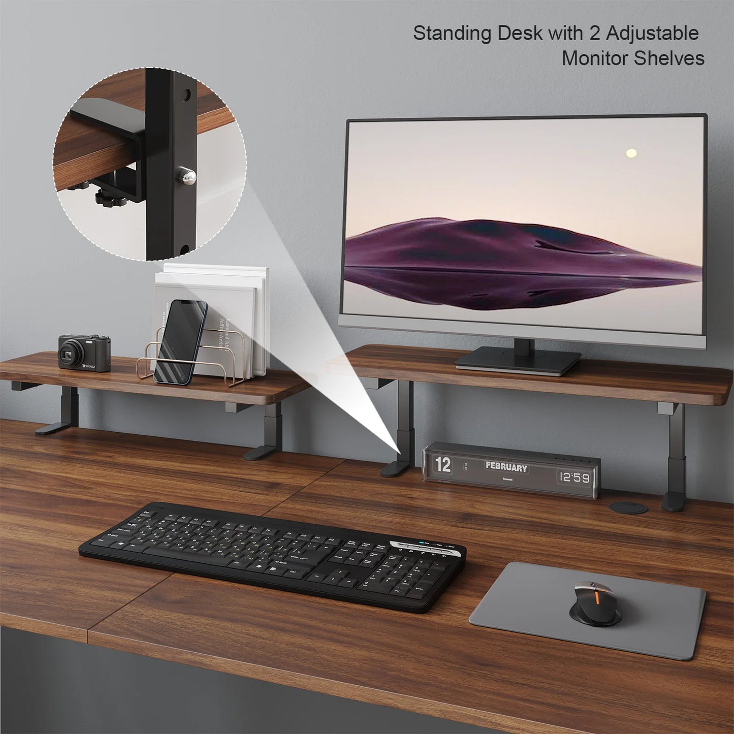 The Standing Desk w/ 2 Adjustable Monitor Shelves Electric Stand Up Desk holds a monitor, camera, phone, and organizer. A keyboard, mouse, and mouse pad are on the wooden surface. A digital clock shows February 12, 12:59.
