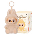 A Cute Labubu The Monsters Box Toy Sweetheart Vinyl Doll in Style F with box, featuring a plush keychain with a round face, big eyes, wide grin, and tan bunny costume. Comes in matching illustrated packaging reading “Have A Seat.”.