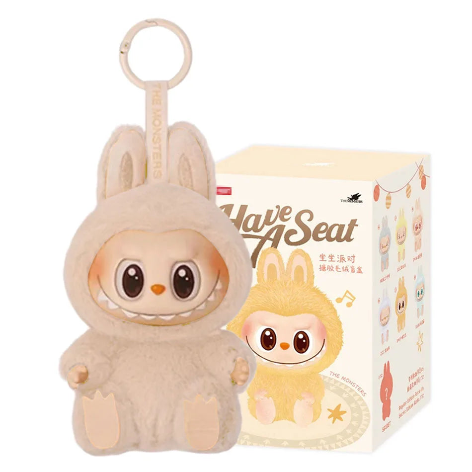 A Cute Labubu The Monsters Box Toy Sweetheart Vinyl Doll in Style F with box, featuring a plush keychain with a round face, big eyes, wide grin, and tan bunny costume. Comes in matching illustrated packaging reading “Have A Seat.”.