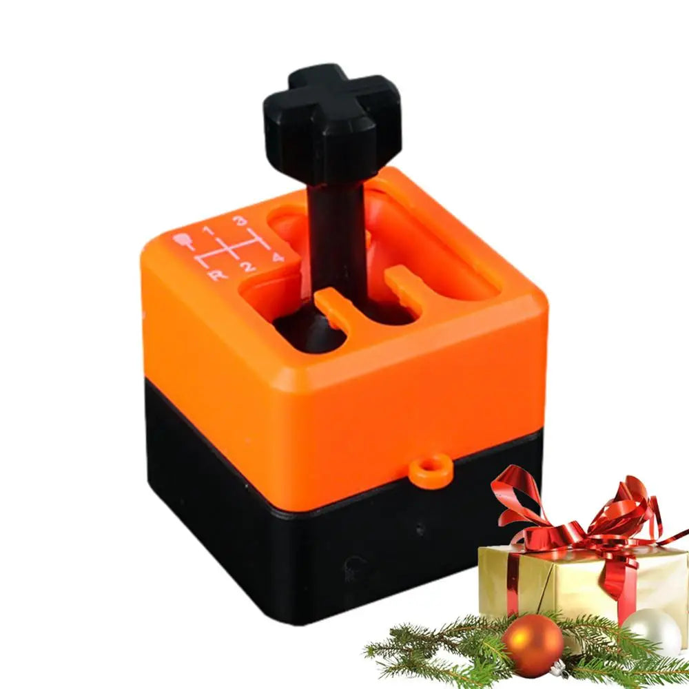 An orange Manual Gear Shifter Keychain 3D Printed Fidget Toy, shaped like a car gear shifter, sits next to a wrapped gift and Christmas ornaments with pine branches. It’s a novelty mood enhancer for office, school, or outdoor use.
