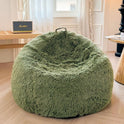 A sage green Faux Fur Comfy Bean Bag Cover (No Filler Storage Chair) sits on a wooden floor in a cozy room with light walls and curtains. Nearby tables hold a radio, while natural light from the window highlights the plush seating.
