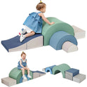 A toddler climbs and sits on the Rainbow Soft Play Set—earthtone foam blocks in ramp, arch, and rectangle shapes with a foldable slide—perfect indoor climbing and crawling toys for boys and girls.