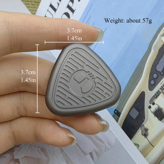 A hand holds an EDC Fingertip Toys Fidget Slider, a small triangular magnetic metal spinner with raised patterns and a mouse icon. Size: 3.7 cm per side, weight: 57 g. A magazine is in the background. Made in Mainland China.