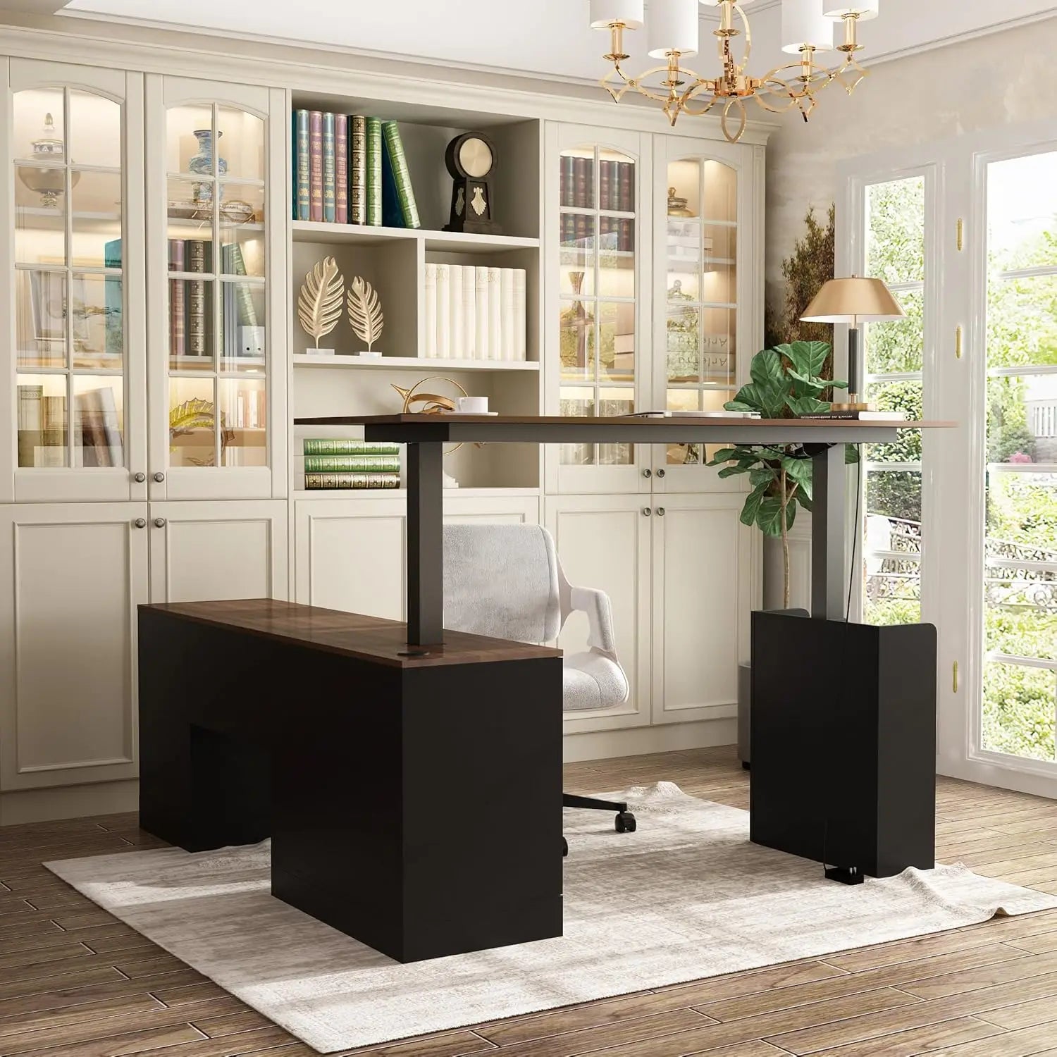 A home office featuring the walnut/black L Shaped Electric Standing Desk with drawers and shelves, a light gray chair, large bookshelf with glass doors, decorative accents, chandelier, potted plant, and abundant natural light from French doors.