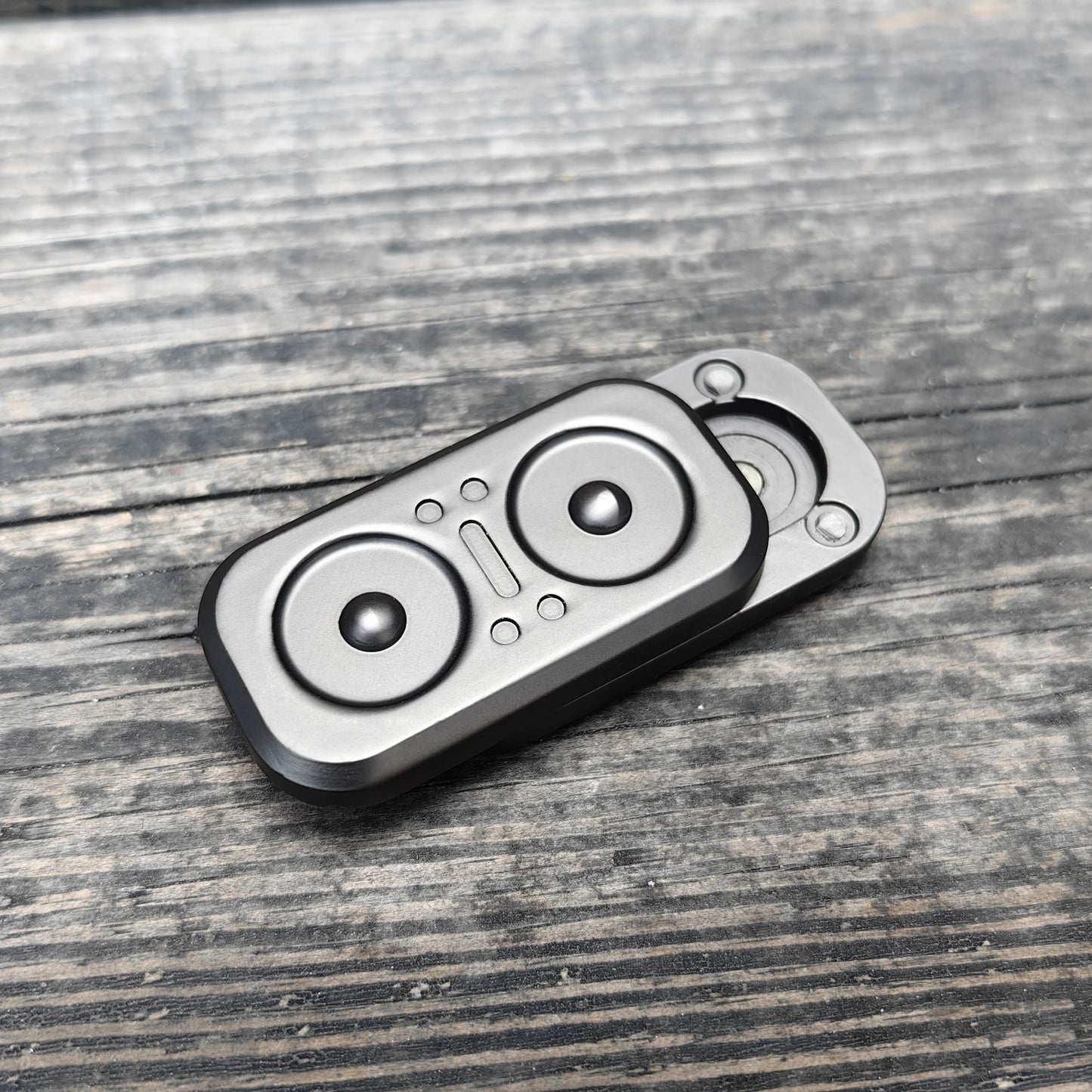 A compact, rectangular Owl Push Slider metal fidget toy with circular accents rests on a weathered wooden surface. Made in Mainland China, this adult EDC haptic slider can be spun or pushed for decompression and stress relief.