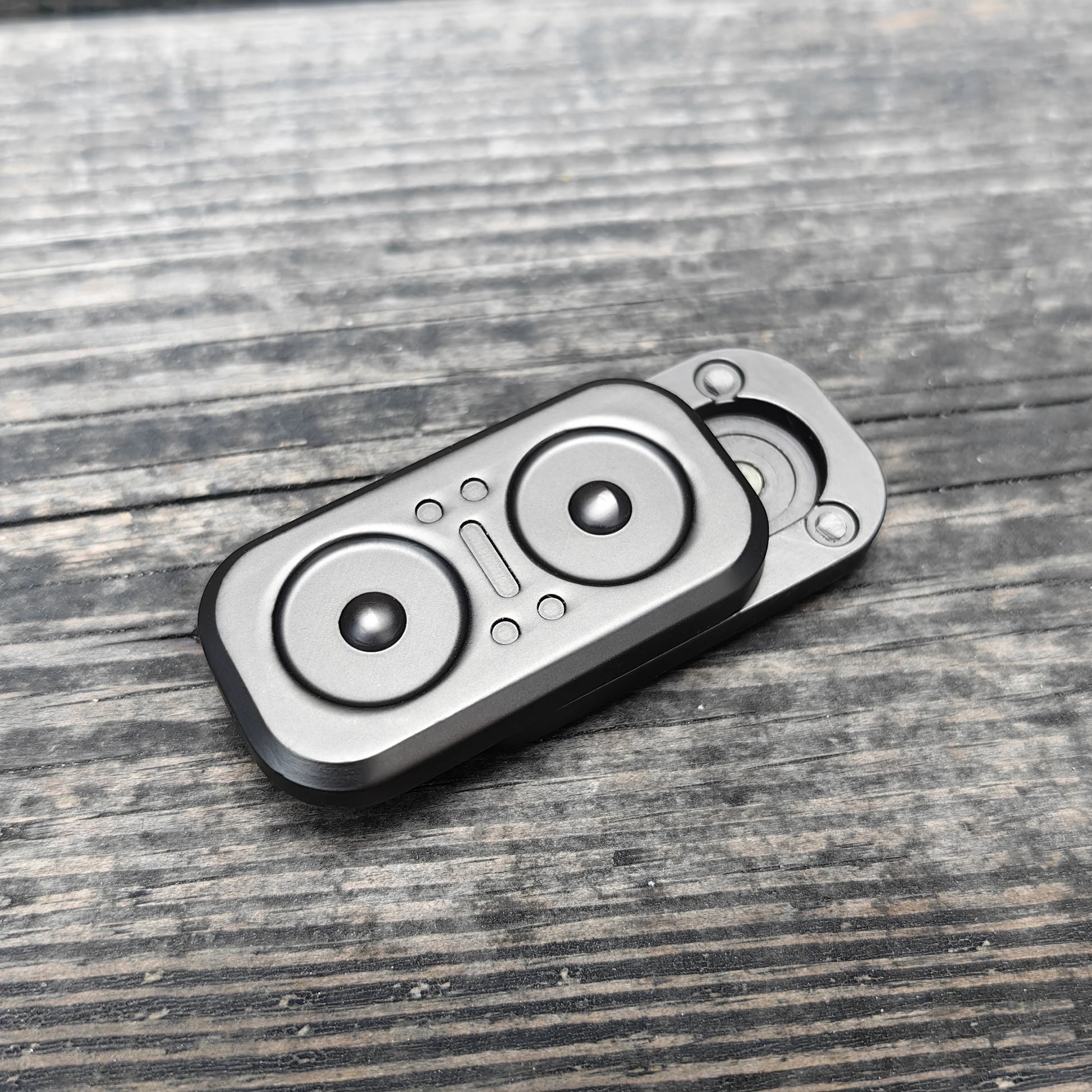 A compact, rectangular Owl Push Slider metal fidget toy with circular accents rests on a weathered wooden surface. Made in Mainland China, this adult EDC haptic slider can be spun or pushed for decompression and stress relief.