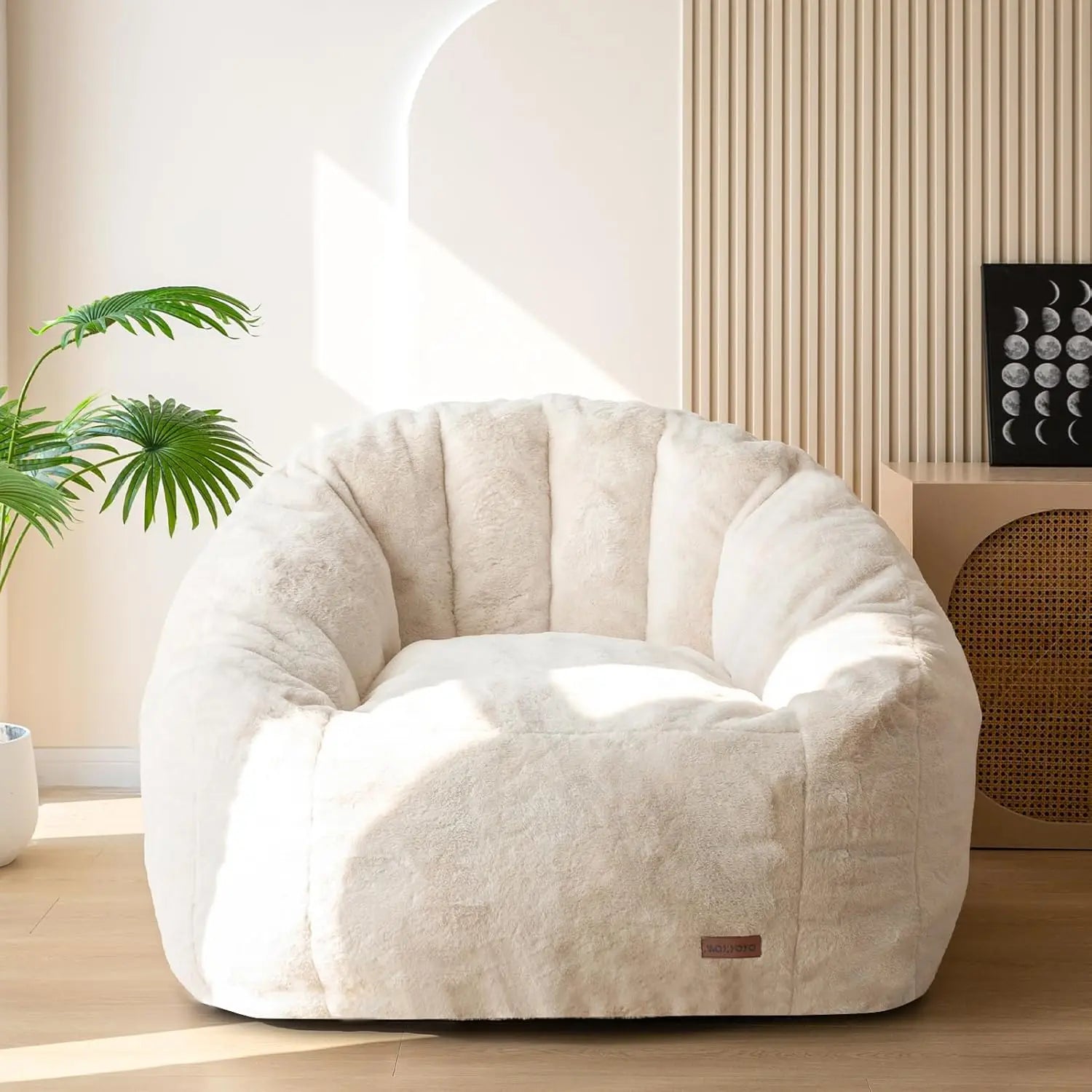 The Giant Bean Bag Chair, an oversized faux fur shell-shaped seat for adults and kids, is shown in a sunlit room with wooden floors, a potted plant, and moon phase wall art. Made in the USA. No assembly required.