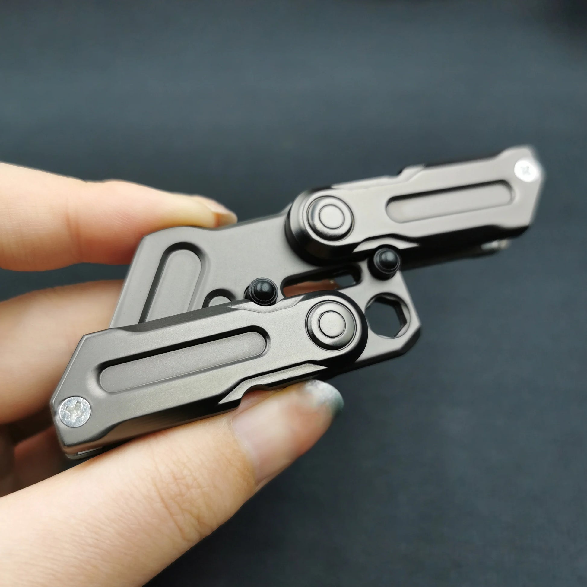 A hand holds the Fidget Magnetic Coin EDC, a sleek metallic multitool with two folding parts, designed for stress relief and anxiety reduction as a multifunctional crowbar fidget slider spinner, set against a black background.