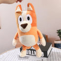 A 17cm Bluey and Bingo Family plush toy cartoon dog hangs above a table with an open black-and-white book, potted plant, and checked cloth—perfect for fans of the stuffed soft dolls and great as birthday or Christmas gifts.