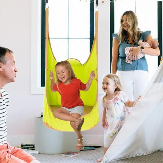 A smiling girl swings indoors in the Kids Pod Swing Seat Bag Sensory Swing Portable Hammock Chair Inflatable Swing With Cushion, while her family—man, woman with baby, and another young girl—watch and smile in a cozy, bright room.