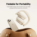 The Edifier ES850NB Wireless Noise Cancelling Bluetooth Headphones with Hi-Res audio and carry bag are displayed above a gold smartphone and open brown travel bag, showcasing their foldable design for easy, portable travel.