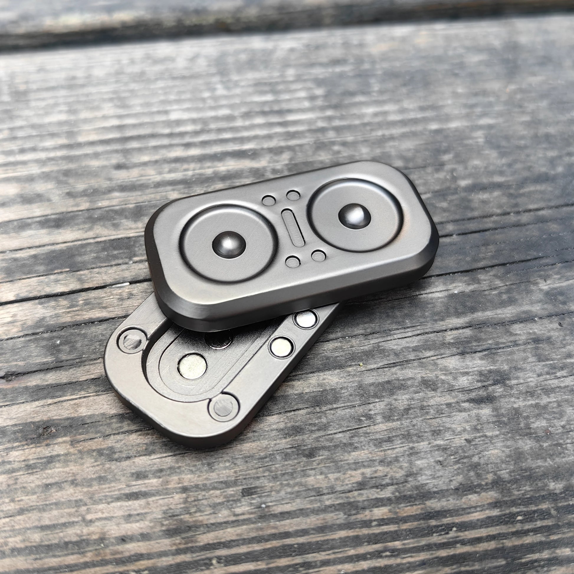 Two Owl Push Slider Fidget Toys with circular, speaker-like designs rest on a weathered wooden surface; one is stacked slightly askew atop the other.