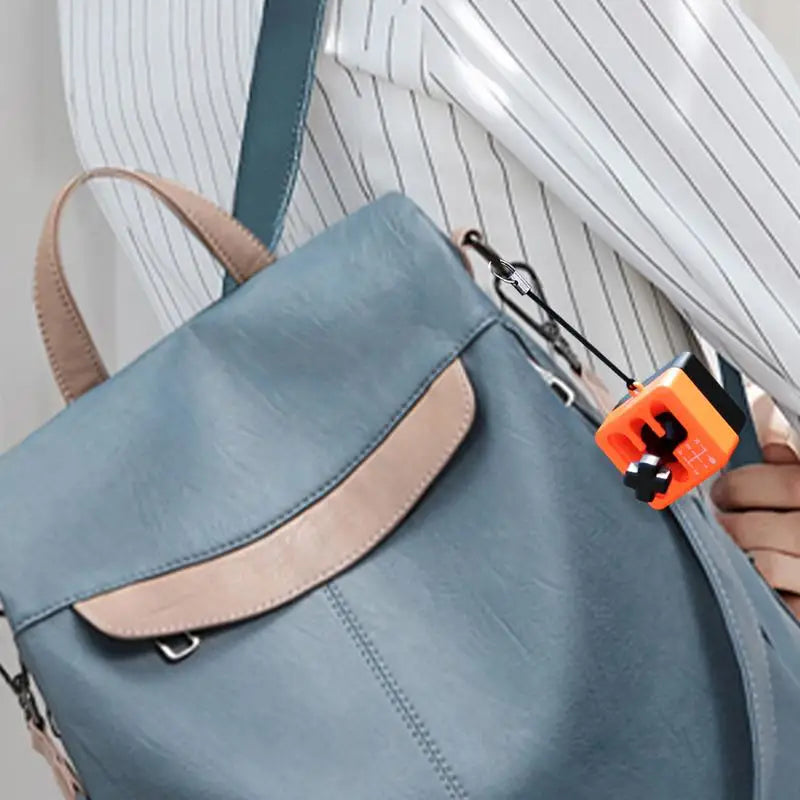 A person in a white striped shirt carries a blue MINOCOOL handbag with tan accents. Attached to the bag’s strap is a Manual Gear Shifter Keychain, a 3D printed fidget toy and mood enhancer for office, school, or outdoor use.