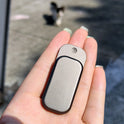 A hand with light green nails holds an Owl Push Slider Fidget Toy outdoors, with a blurry cat in the background on sunlit pavement.