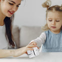 A woman and a young girl sit at a table. The girl, in a blue dress, reaches toward a silver Infinity Gear Cube Spinner Antistress Toy held by the smiling woman.