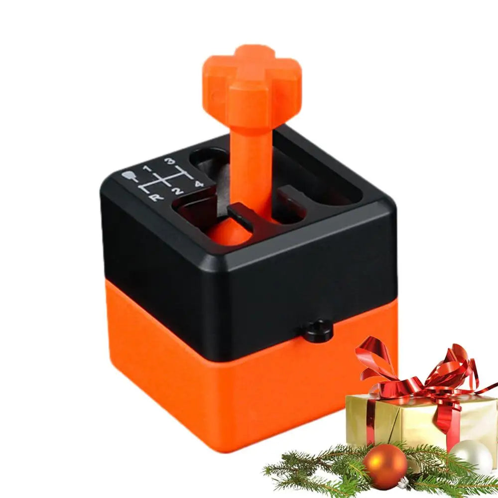 A black Manual Gear Shifter Keychain 3D Printed Fidget Toy sits beside a decorated Christmas present with ornaments and pine branches in the foreground. Made from chemical-free materials for safe play.