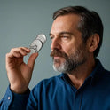 A bearded man in a blue shirt holds the Fidget Slider Magnetic Metal Spinner Toy up to his right eye, peering through it thoughtfully as if planning his next adventure, with a plain background behind him.