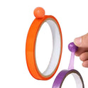 A hand pulls purple Sticky Toys For Kids Multifunctional Sticky Ball Tapes from a roll, with a purple ball at the end; an orange roll with its own ball sits nearby—fun sensory fidget toys perfect for creative travel activities for all ages.
